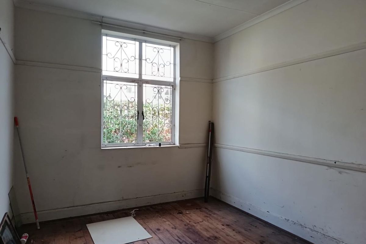 An empty bedroom featuring original timber flooring, security bars on the window, and classic picture rails, ready for renovation and personalization.