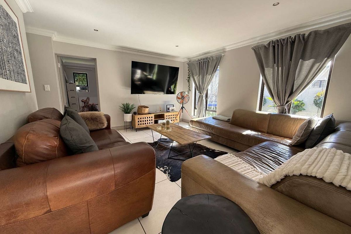 A spacious living room featuring large windows, tiled flooring, and recessed ceiling lighting, creating a bright and comfortable atmosphere.