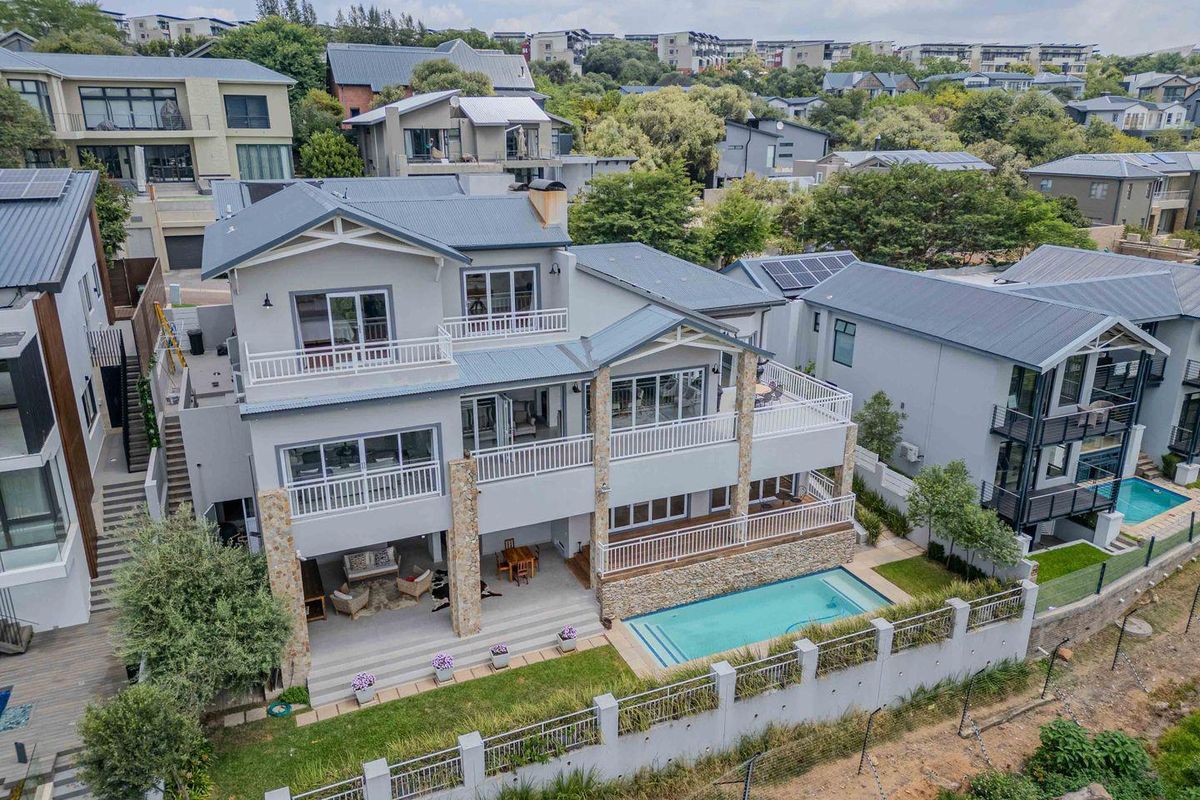 Aerial view of a multi-level residential property featuring a swimming pool, covered patio, balconies, and stone-clad architectural detailing.