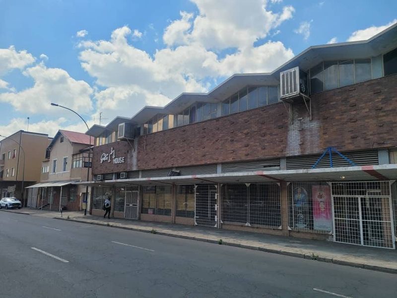 Street-level view of a commercial building featuring a brick facade, sawtooth roofline, and secure display windows with integrated security grilles.