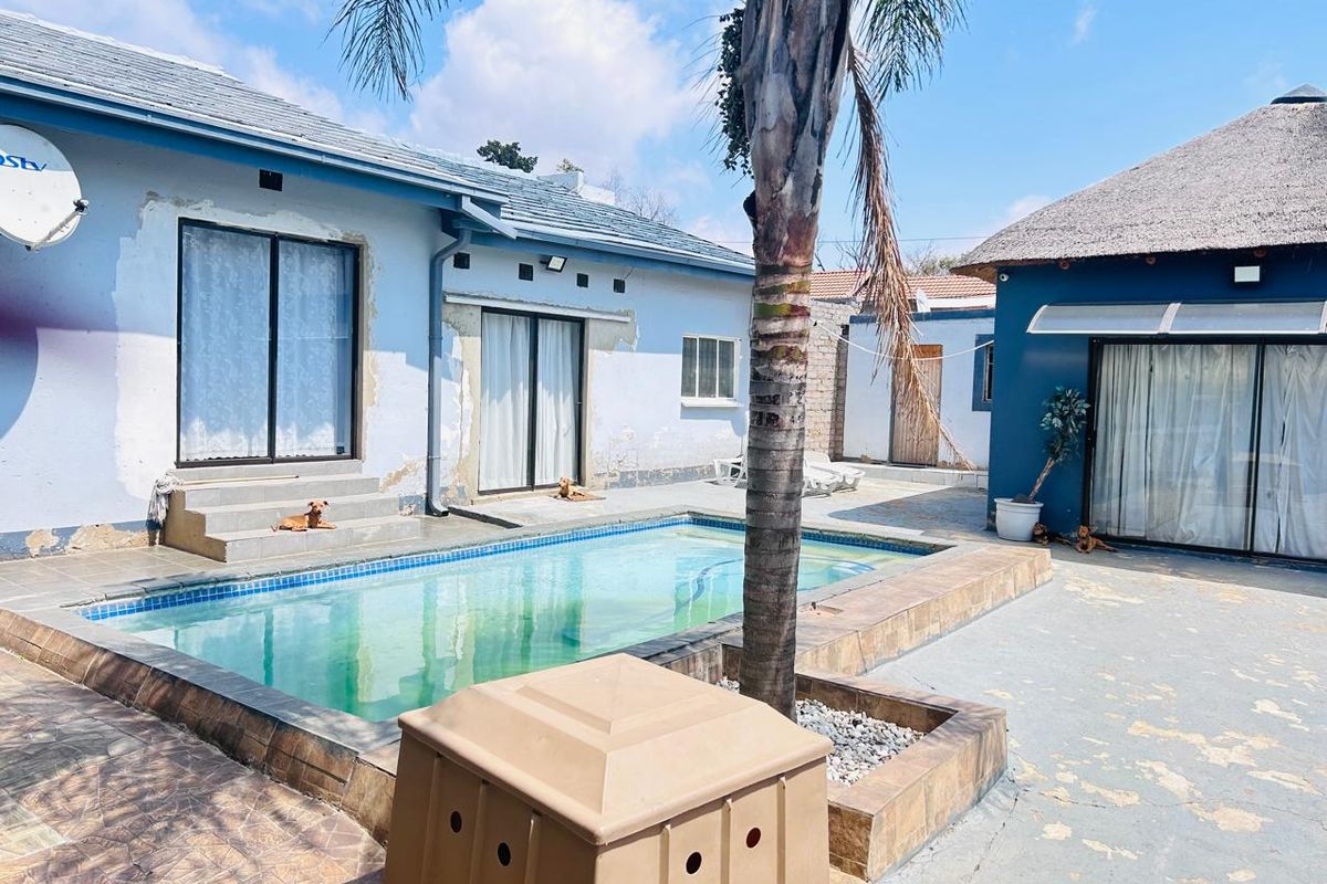 Outdoor pool area featuring a swimming pool with tiled surround, adjacent to building structures with sliding glass doors and a thatched roof section.