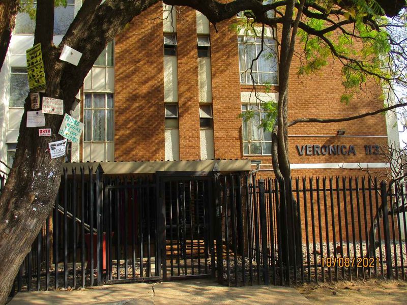 Front exterior view of the Veronica apartment building featuring a brick facade, metal security gate, and perimeter fencing.