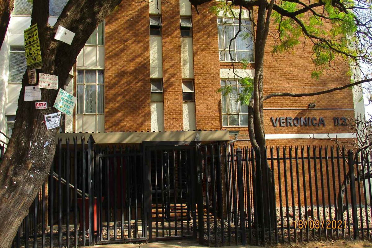 Front exterior view of the Veronica apartment building featuring a brick facade, metal security gate, and perimeter fencing.