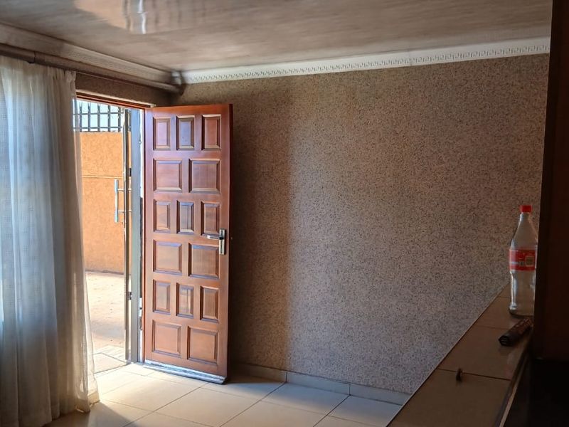 An empty living area featuring tiled floors, textured walls, and a wooden door leading to an outdoor space.