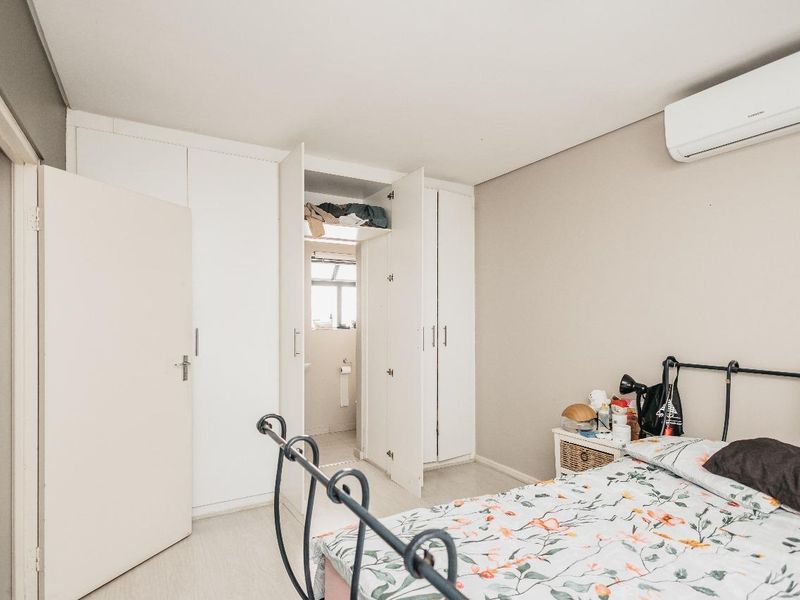 A well-maintained bedroom featuring built-in cupboards, a wall-mounted air conditioning unit, and direct access to an en-suite bathroom.