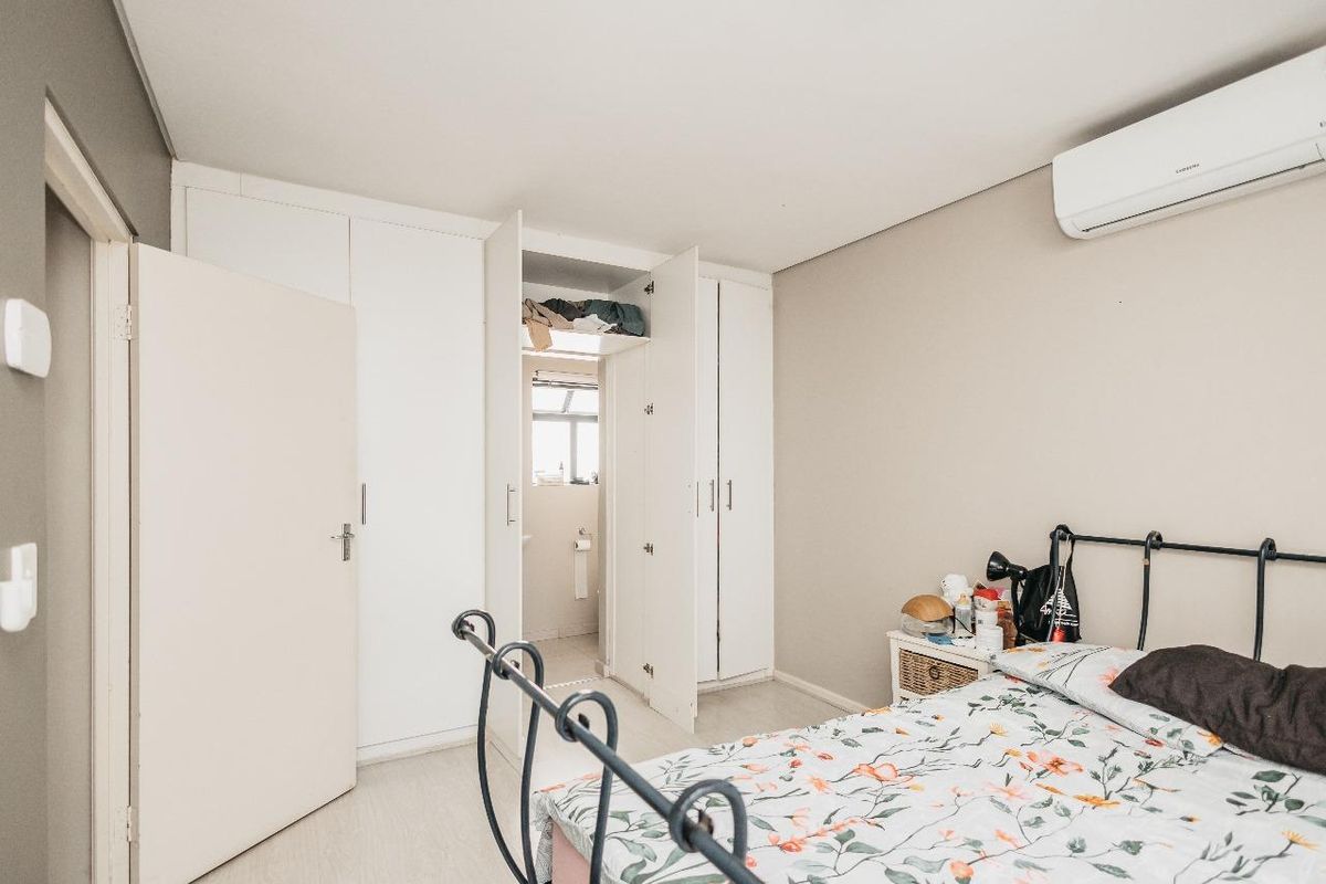 A well-maintained bedroom featuring built-in cupboards, a wall-mounted air conditioning unit, and direct access to an en-suite bathroom.