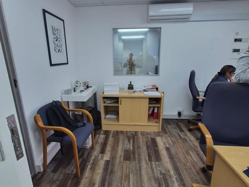 A functional office space featuring laminate wood-look flooring, a suspended ceiling with recessed lighting, and a wall-mounted split-system air conditioning unit.