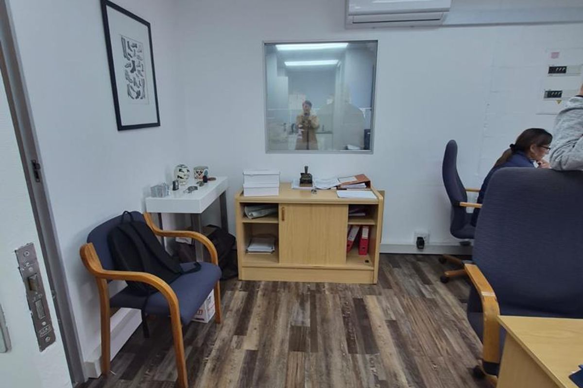 A functional office space featuring laminate wood-look flooring, a suspended ceiling with recessed lighting, and a wall-mounted split-system air conditioning unit.