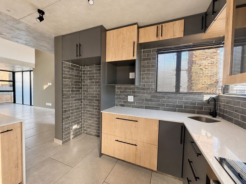 Modern kitchen featuring two-tone cabinetry, stone countertops, subway tile backsplash, and an exposed concrete ceiling, offering a contemporary and functional culinary space.