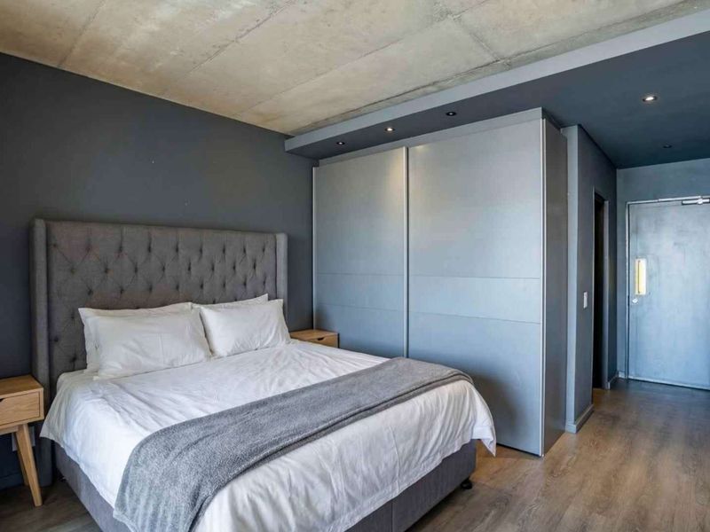 Modern bedroom featuring an exposed concrete ceiling, built-in sliding door wardrobes, recessed lighting, and durable laminate flooring.