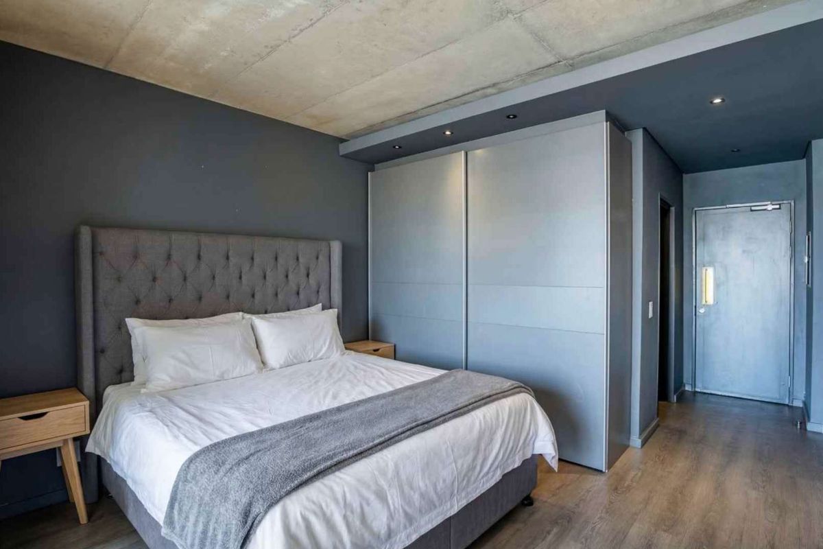 Modern bedroom featuring an exposed concrete ceiling, built-in sliding door wardrobes, recessed lighting, and durable laminate flooring.