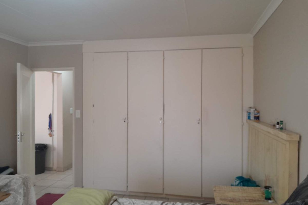 A bedroom featuring a large wall of built-in cupboards with a neutral finish, providing ample storage space.