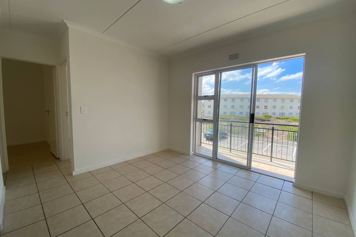 A bright, empty living area featuring tiled flooring and large sliding glass doors that open onto a private balcony.