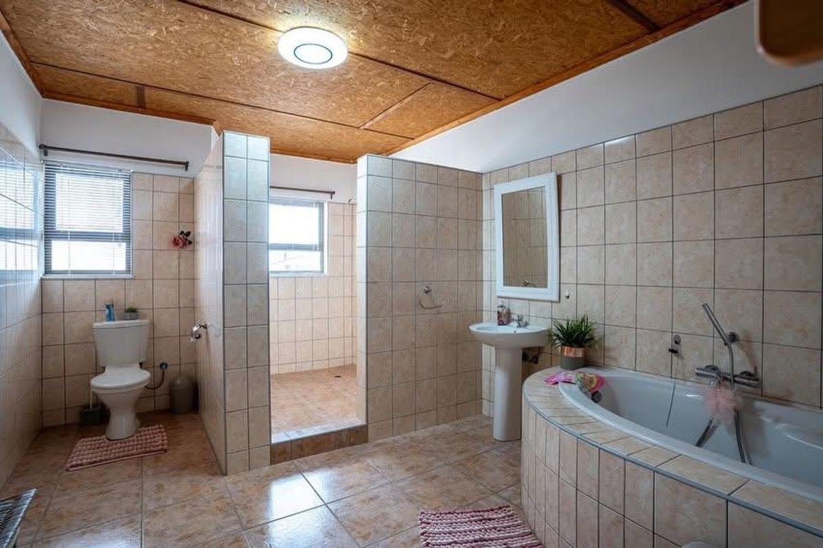 Spacious bathroom featuring a walk-in shower, built-in bathtub, pedestal basin, and toilet, finished with neutral wall and floor tiling.