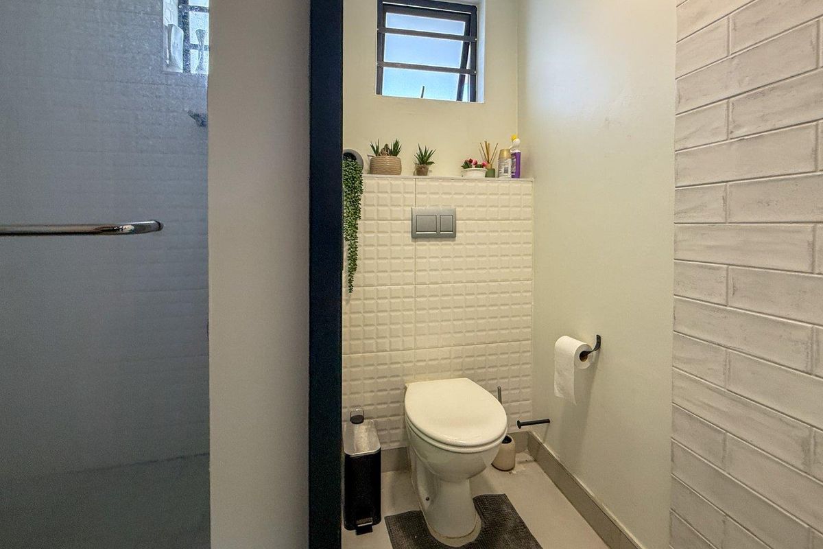 A compact bathroom featuring a wall-mounted toilet with a concealed cistern, textured feature tiling, and a glass shower enclosure.