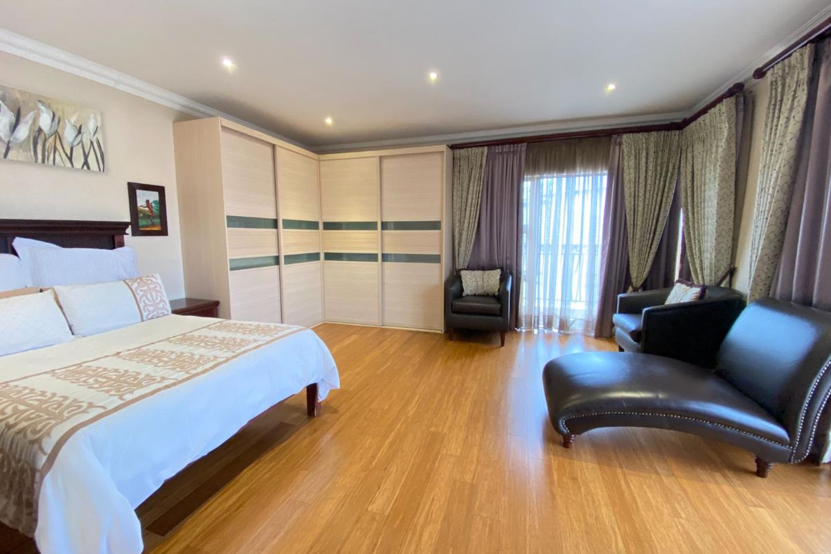 Spacious bedroom featuring light wood-tone laminate flooring, extensive built-in cupboards, recessed lighting, and direct access to a private balcony through sliding glass doors.