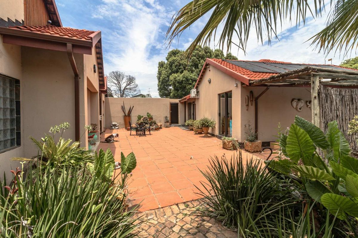 A spacious rear courtyard featuring terracotta tiled flooring, established garden beds, and a covered patio area, providing a private outdoor living space.