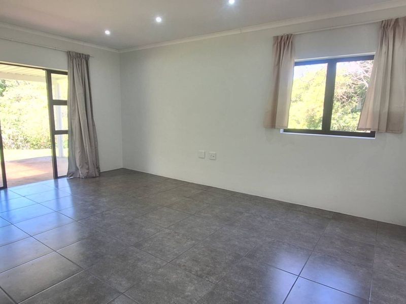 A bright, empty living room featuring neutral tiled flooring, recessed lighting, and a sliding glass door providing access to the outdoor area.