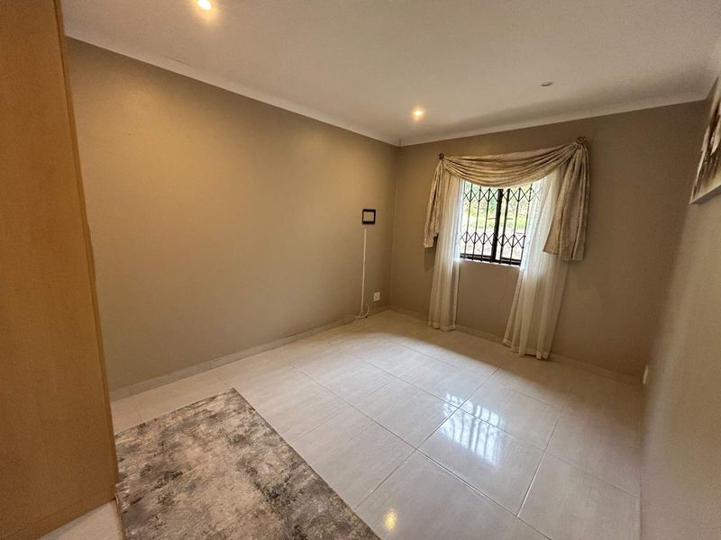 A clean, neutral-toned bedroom featuring tiled flooring, recessed downlighting, and a built-in cupboard, offering a versatile space ready for personalization.