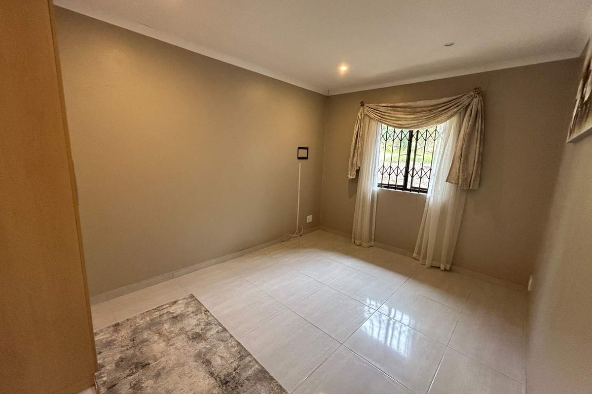 A clean, neutral-toned bedroom featuring tiled flooring, recessed downlighting, and a built-in cupboard, offering a versatile space ready for personalization.