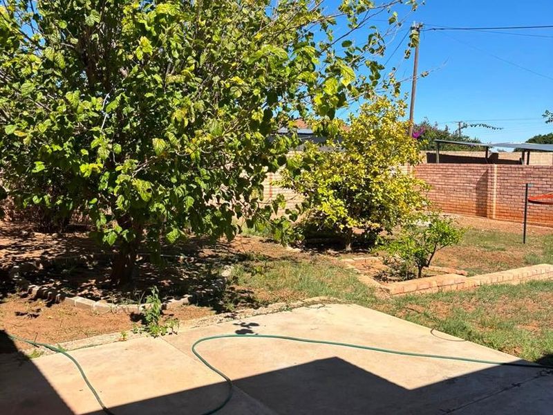A spacious rear garden featuring a concrete patio area, mature trees, and brick boundary walls, offering potential for landscaping and outdoor living improvements.