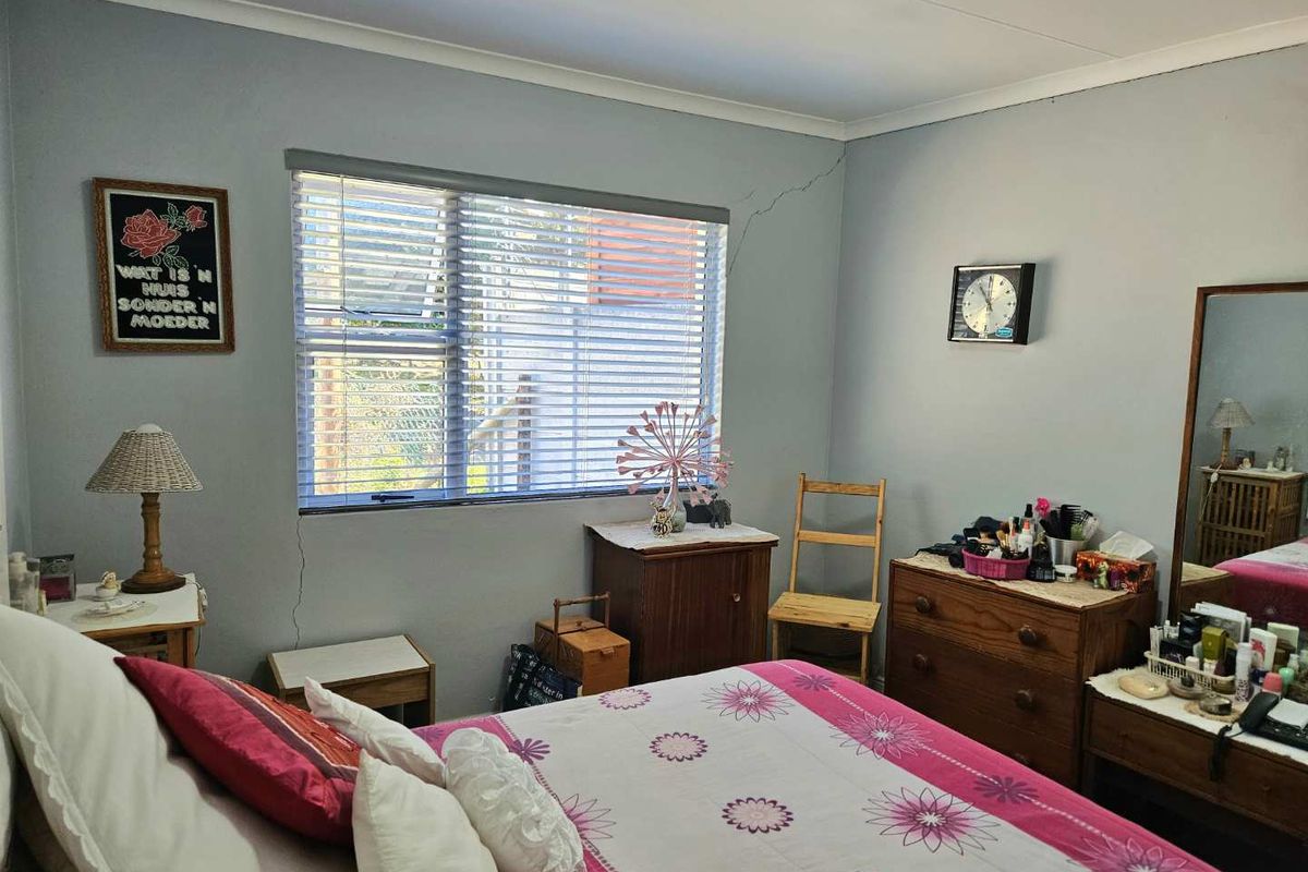 A bedroom featuring a window with horizontal blinds and visible wall cracking near the window frame.