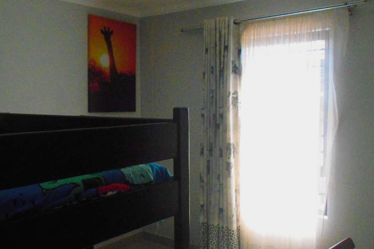 A bedroom featuring tiled flooring and coved ceiling details, with natural light entering through a window dressed with curtains.