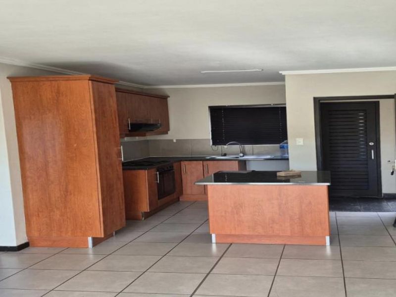 Spacious kitchen featuring wooden cabinetry, a central island, built-in oven, extractor fan, and tiled flooring throughout.
