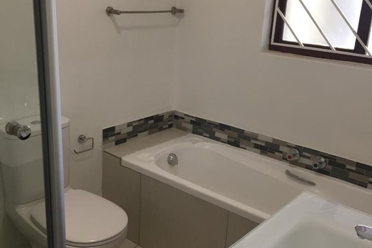 A clean, functional bathroom featuring a bathtub, vanity basin, toilet, and tiled finishes with a mosaic splashback detail.