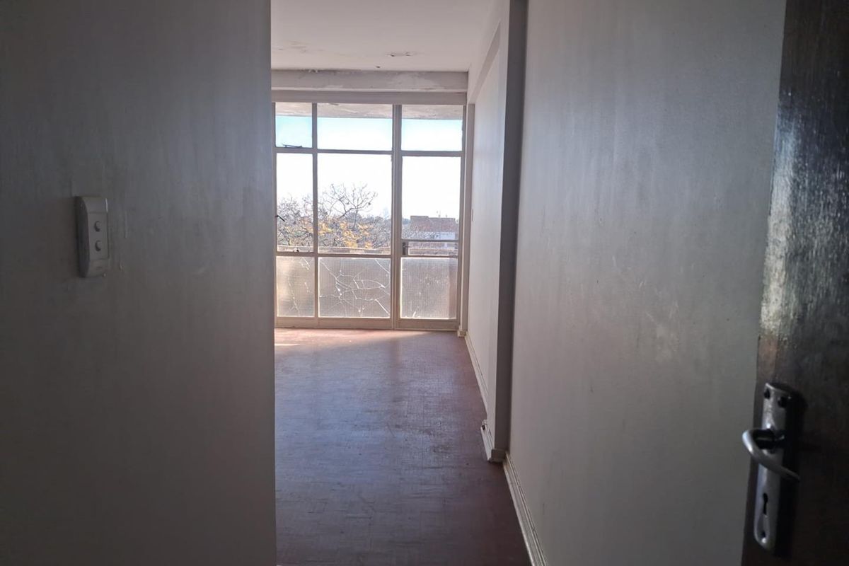 An empty living room featuring parquet flooring and a large glass sliding door leading to an exterior area, requiring cosmetic updates and repairs.