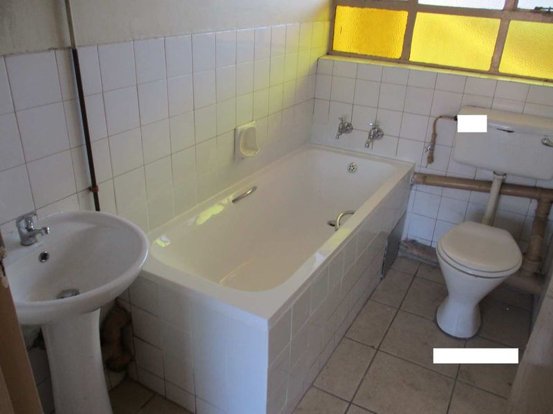 A dated bathroom featuring a pedestal basin, built-in bathtub, and toilet with exposed plumbing and original ceramic tiling throughout.