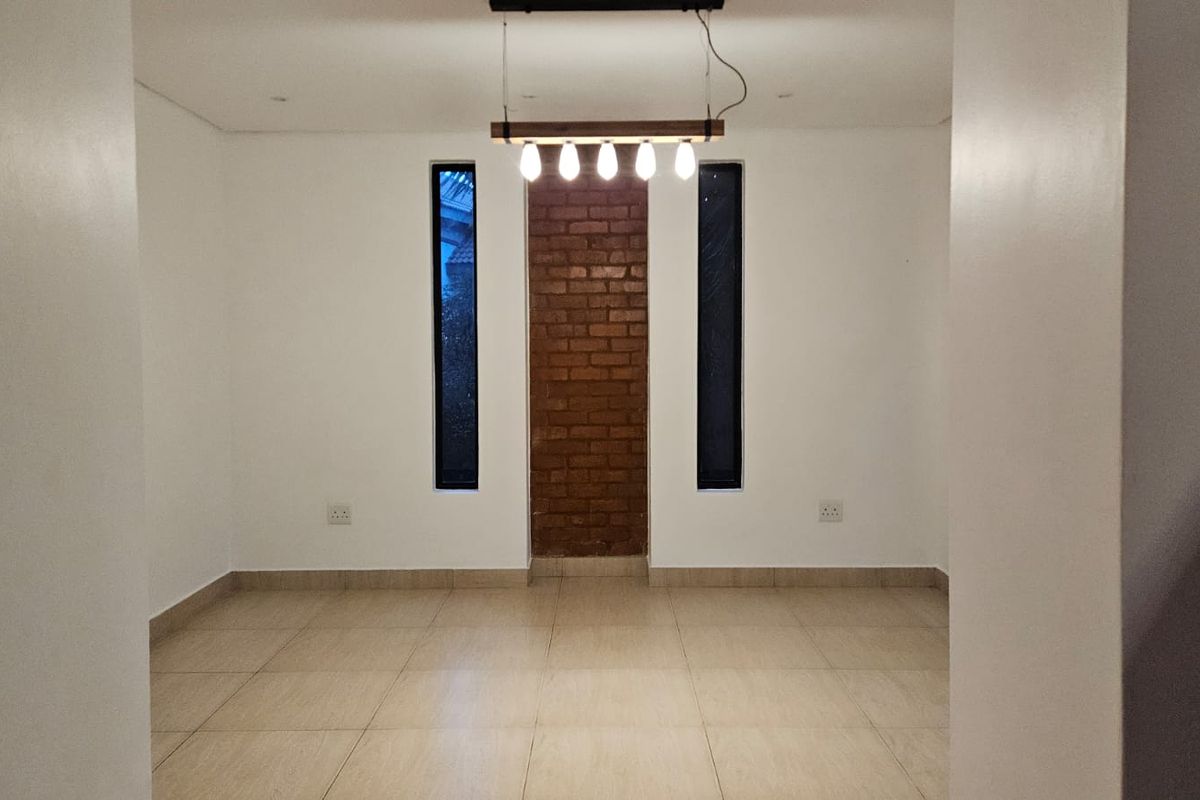 An empty living area featuring tiled flooring, a central exposed brick accent wall, vertical windows, and a modern pendant light fixture.