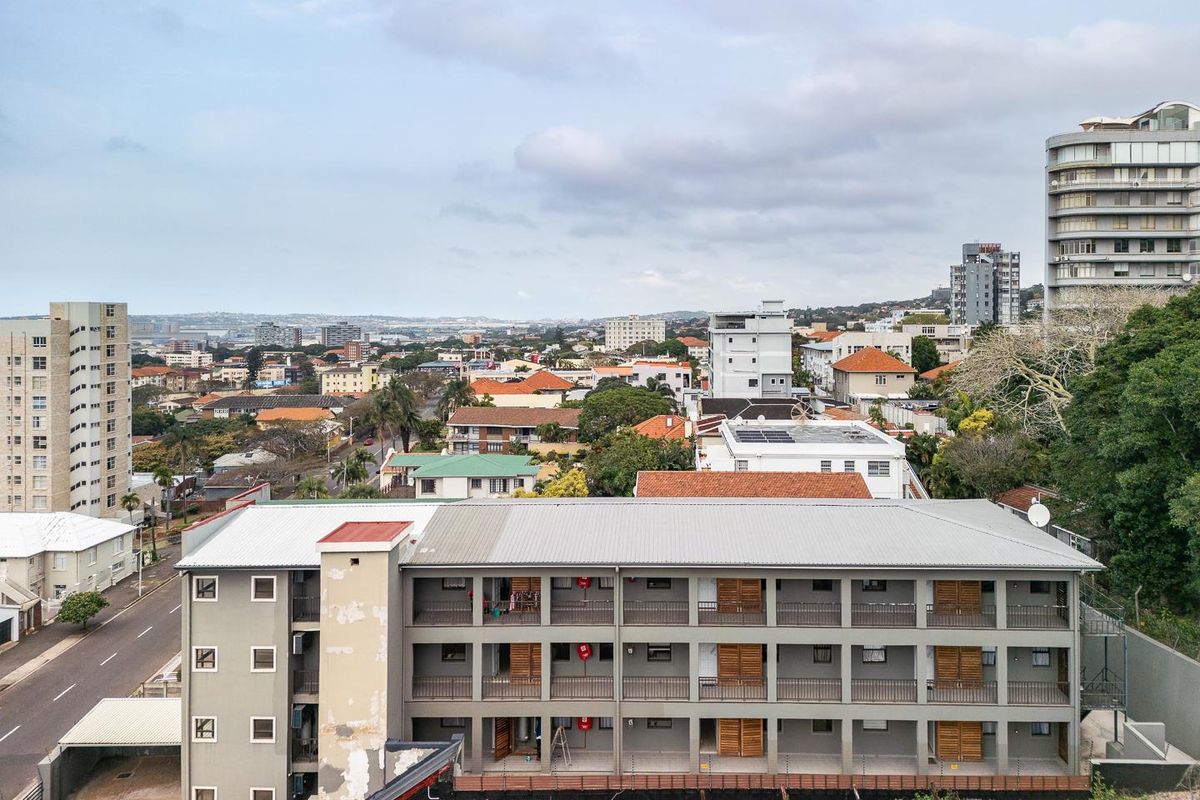 Aerial view of an apartment complex featuring a metal roof, multi-level balcony access, and perimeter security fencing in an urban setting.