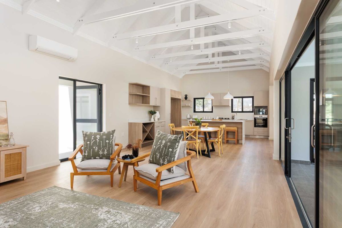 Spacious open-plan living and kitchen area featuring high vaulted ceilings with exposed rafters, modern cabinetry, and seamless access to outdoor spaces.