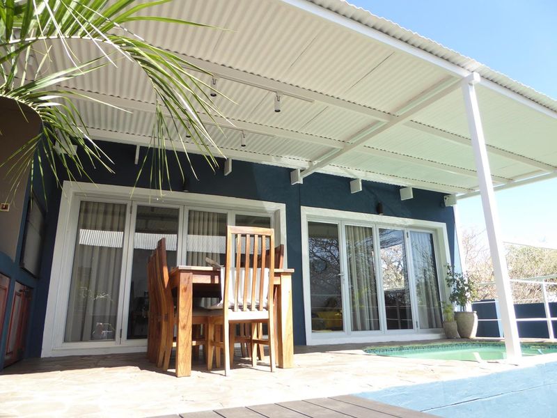 Covered outdoor patio area featuring stone paving, corrugated roofing, and direct access to the swimming pool through sliding glass doors.