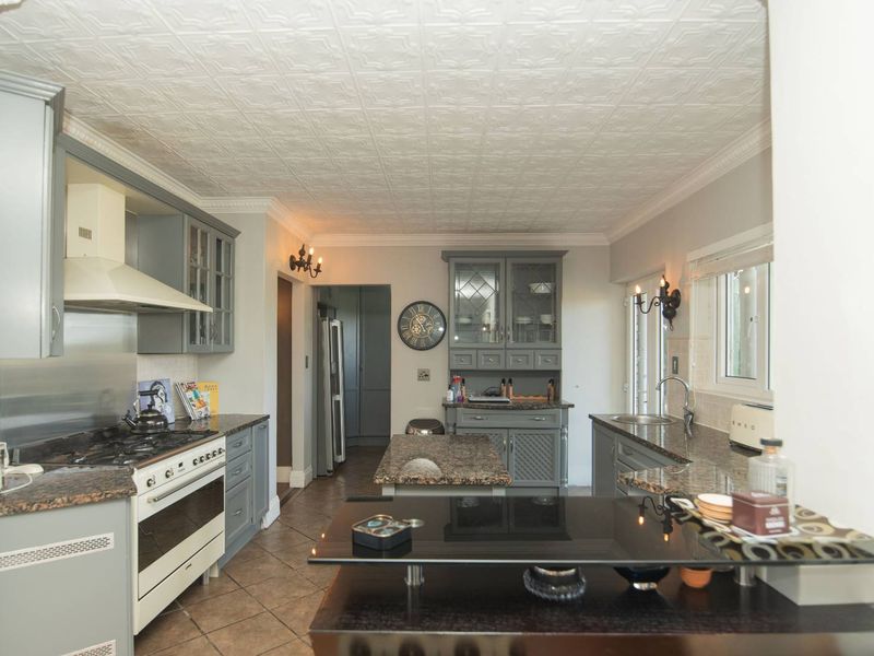 A well-appointed kitchen featuring granite countertops, built-in cabinetry, a gas range with extractor fan, and a decorative pressed ceiling.