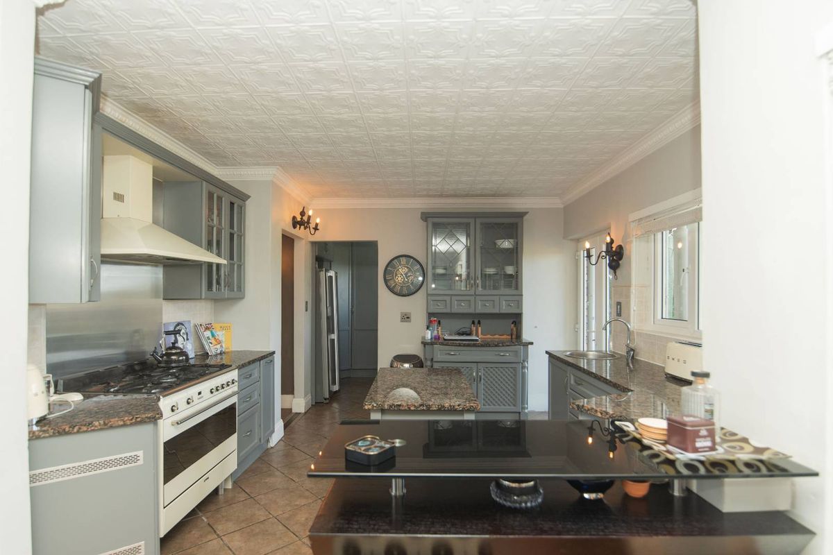 A well-appointed kitchen featuring granite countertops, built-in cabinetry, a gas range with extractor fan, and a decorative pressed ceiling.
