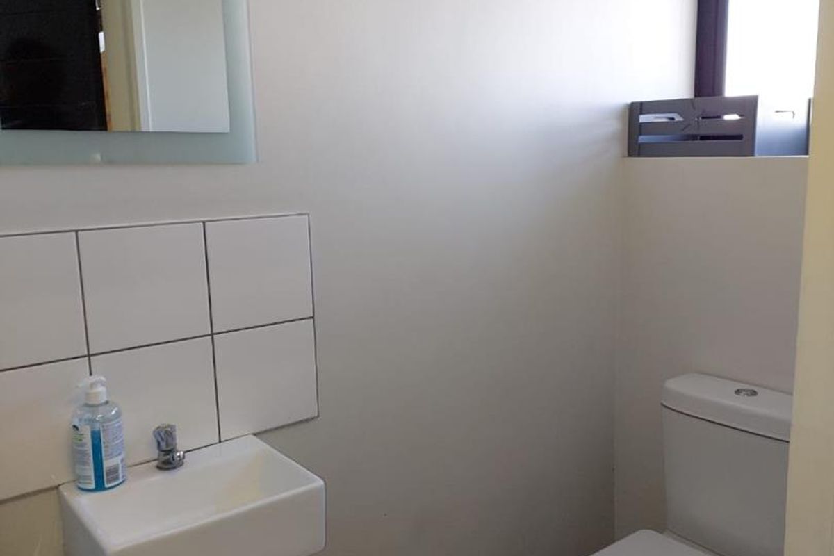 A compact office restroom featuring a wall-mounted basin with tiled splashback and a standard toilet suite.