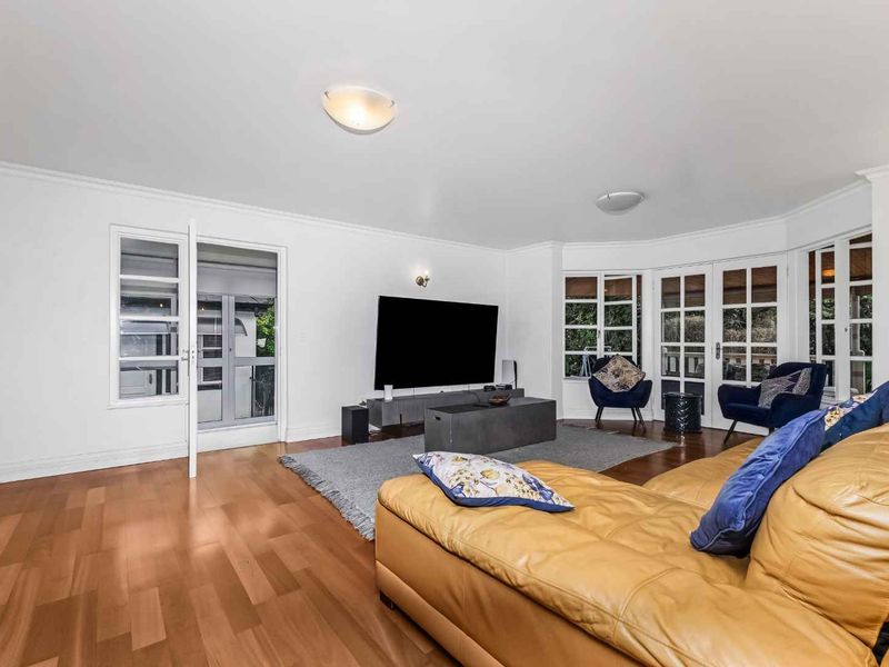 Spacious living room featuring hardwood flooring, large bay windows, and multiple sets of french doors providing ample natural light and garden access.