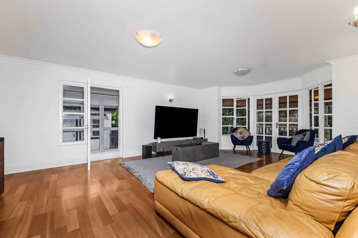 Spacious living room featuring hardwood flooring, large bay windows, and multiple sets of french doors providing ample natural light and garden access.