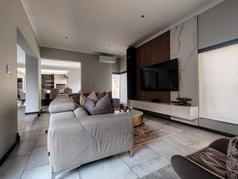 Modern living room featuring a sleek built-in media unit with marble-look accents, recessed lighting, split-system air conditioning, and neutral tiled flooring.
