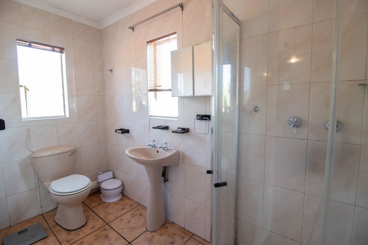 A functional bathroom featuring a pedestal basin, toilet, and glass shower enclosure with neutral wall tiling and floor tiles.