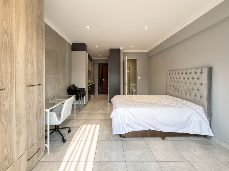 Modern open-plan studio apartment featuring tiled floors, built-in cabinetry, a compact kitchen area, and an en-suite bathroom.