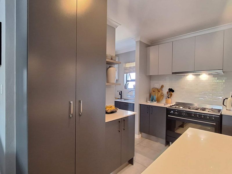 Modern kitchen featuring two-tone cabinetry, stone countertops, a gas stove with extractor fan, and a subway tile backsplash with floating shelving.