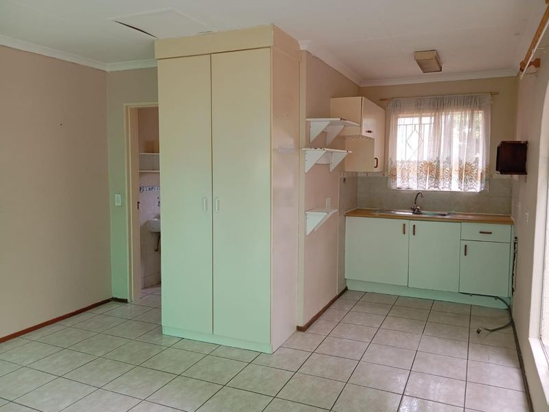 A compact kitchen area featuring tiled floors, built-in cabinetry, and a stainless steel sink, requiring cosmetic updates to modernize the space.