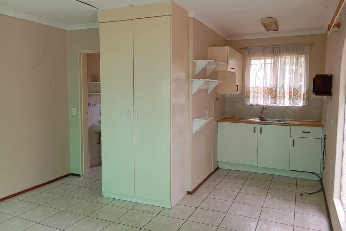A compact kitchen area featuring tiled floors, built-in cabinetry, and a stainless steel sink, requiring cosmetic updates to modernize the space.