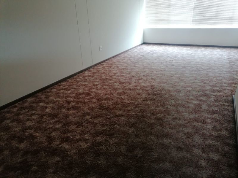 An empty bedroom featuring brown patterned carpeting and fitted venetian blinds, offering a blank canvas for potential interior updates.