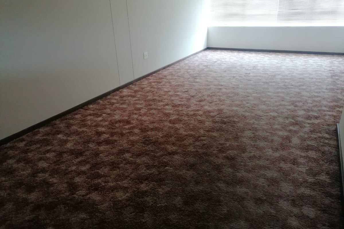An empty bedroom featuring brown patterned carpeting and fitted venetian blinds, offering a blank canvas for potential interior updates.