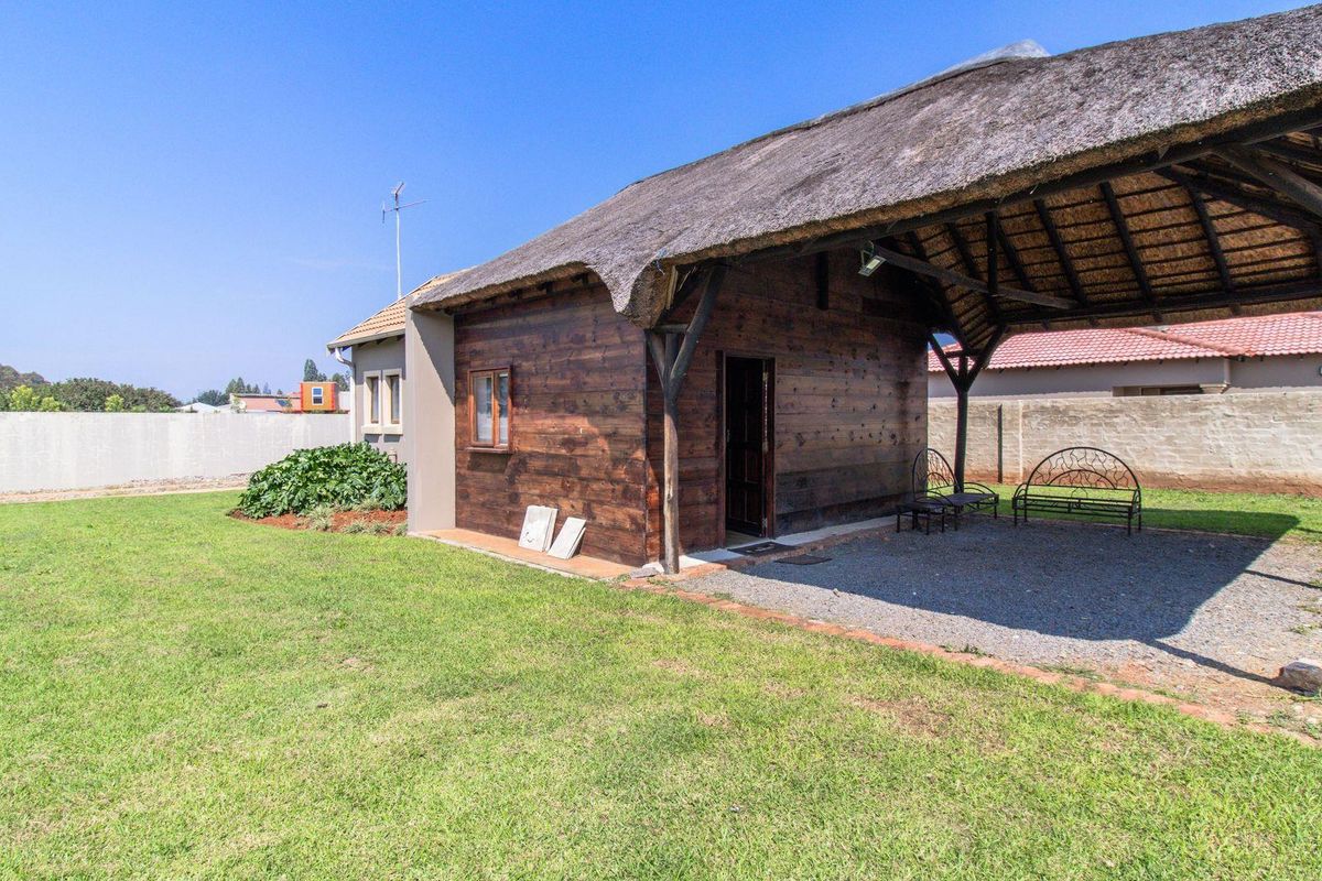 Rear view of a property featuring a thatched roof structure with a covered patio area, timber cladding, and a spacious garden.