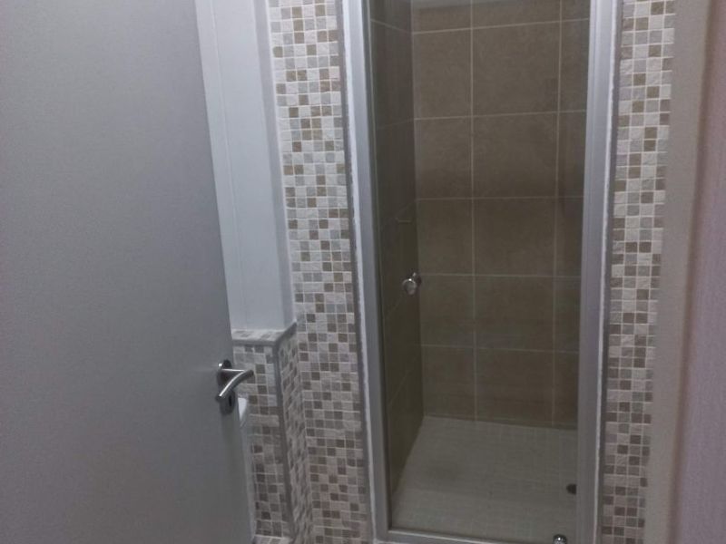 A clean bathroom featuring a glass-enclosed shower with a combination of mosaic and large format neutral-toned wall tiles.